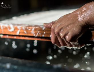 Imagen de mano formando el papel, se aprecia una parte de la forma y mucha pasta de algodón blanco 