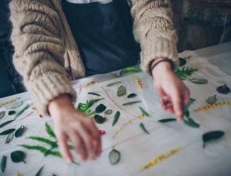 Estampación botánica: Manos colocando hojas y flores sobre un tejido.